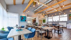 A spacious dining area with wooden tables and chairs, large windows, and hanging pendant lights. - Penzión Čerešnový Sad (Mengusovce)