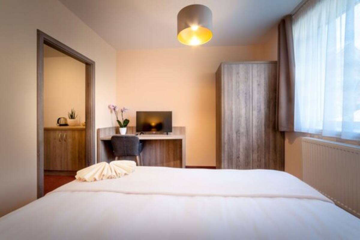 A hotel room with a bed, a desk with a computer, a chair, and a window with curtains.