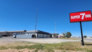 A Super 7 Inn sign, a building with a metal roof, and a clear blue sky. - Super 7 Inn (Midland)