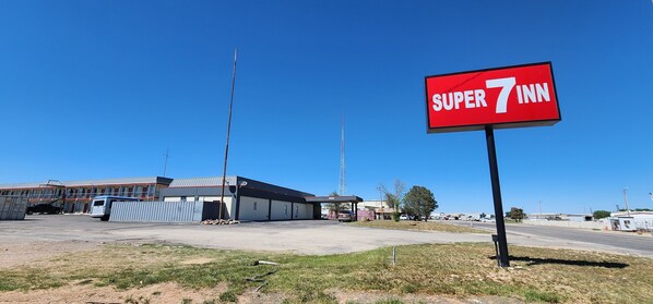 A Super 7 Inn sign, a building with a metal roof, and a clear blue sky. - Super 7 Inn (Midland)