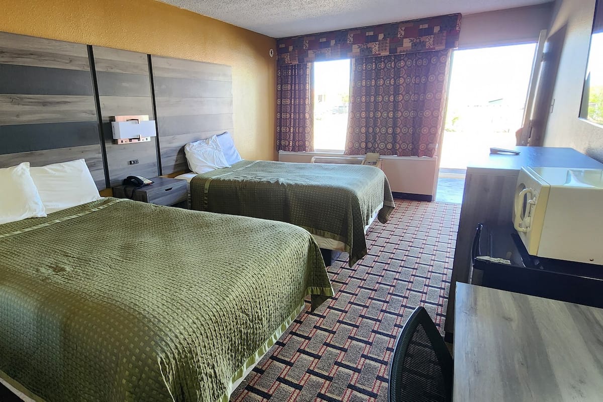 A hotel room with two beds, a desk with a sink, and a television.
