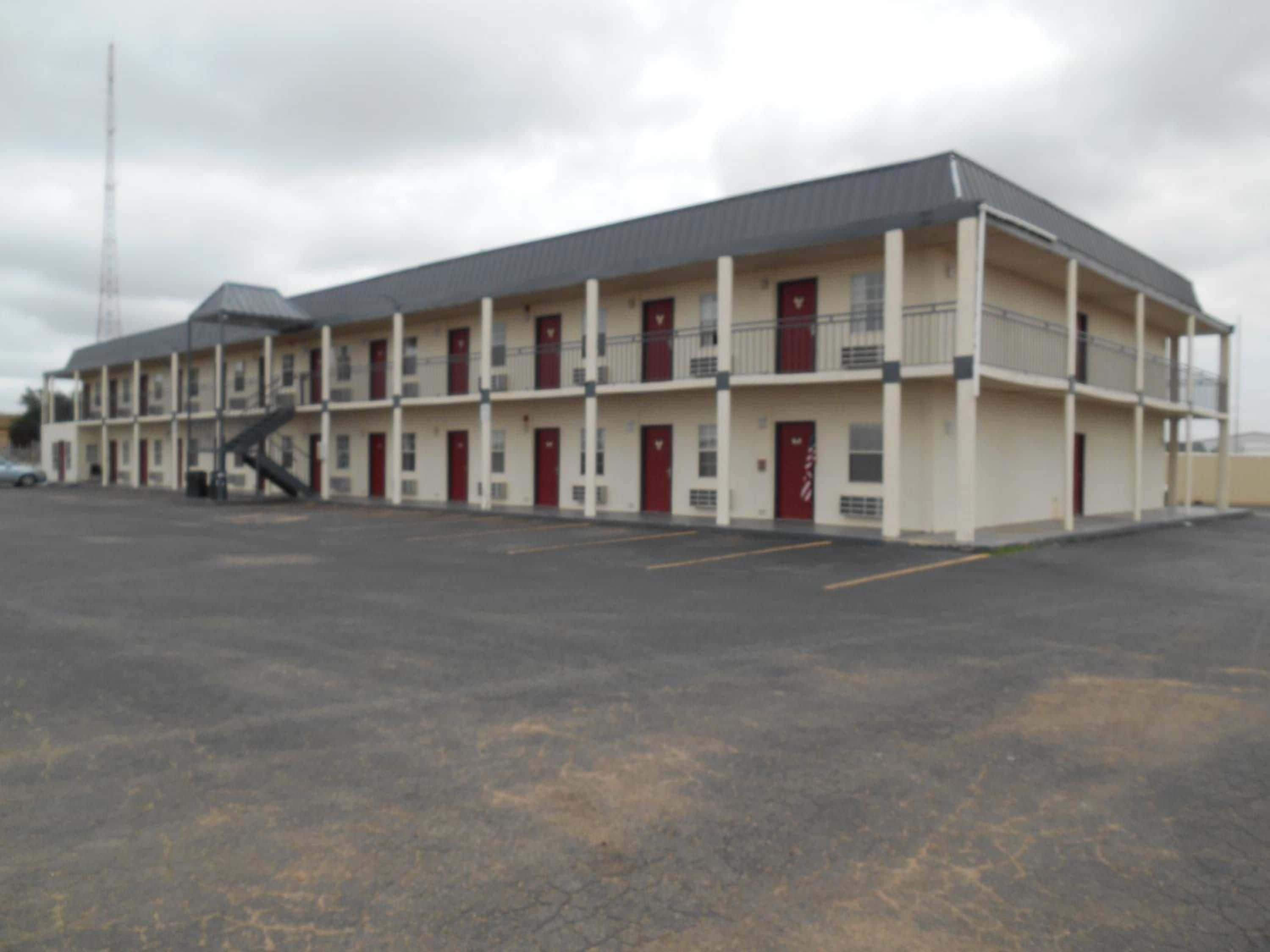 A multi-story motel with a flat roof, multiple balconies, and a parking lot.