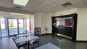 A restaurant interior with tables and chairs, a counter with a menu board, and a view through the glass door. - Super 7 Inn (Midland)