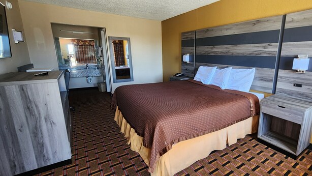 A hotel room with a bed, bedside table, and a desk with a chair. - Super 7 Inn (Midland)