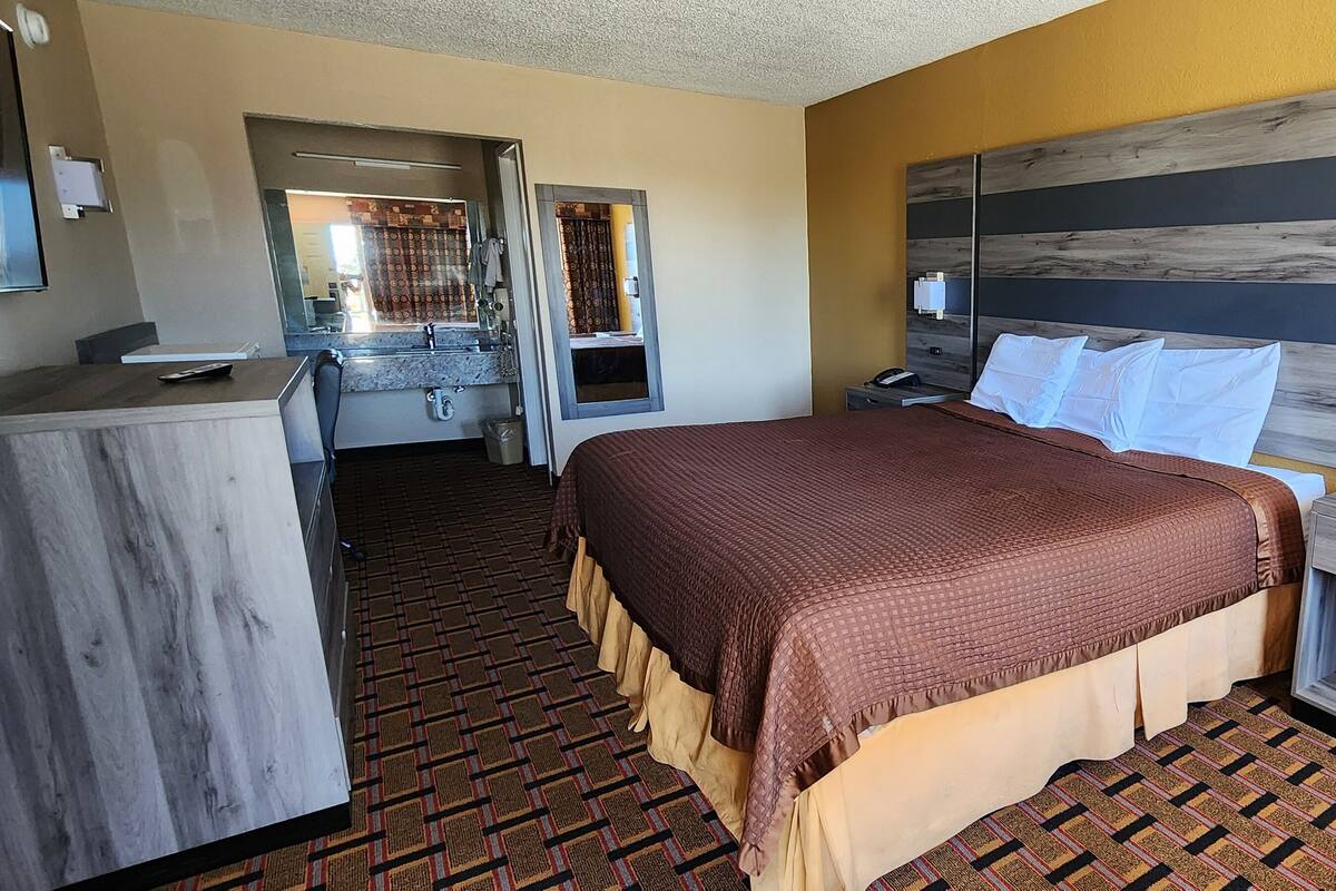 A hotel room with a bed, bedside table, and a desk with a chair.