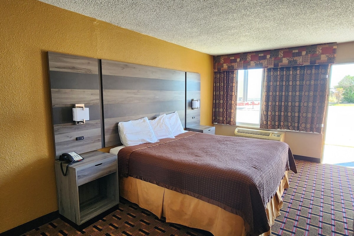 A hotel room with a bed, bedside table, and a window with curtains.