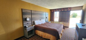 A hotel room with a bed, bedside table, and a window with curtains. - Super 7 Inn (Midland)