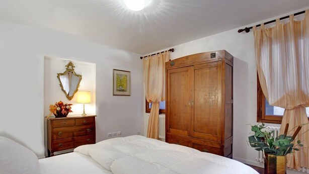 Ein Schlafzimmer mit einem großen Bett, einem Holzschrank, einem Nachttisch mit Lampe und einem Spiegel.