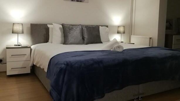A bedroom with a bed, two bedside tables, a nightstand, a wall-mounted picture, and a radiator. - Filton House (Bristol)