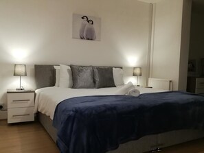A bedroom with a bed, two bedside tables, a nightstand, a wall-mounted picture, and a radiator. - Filton House (Bristol)