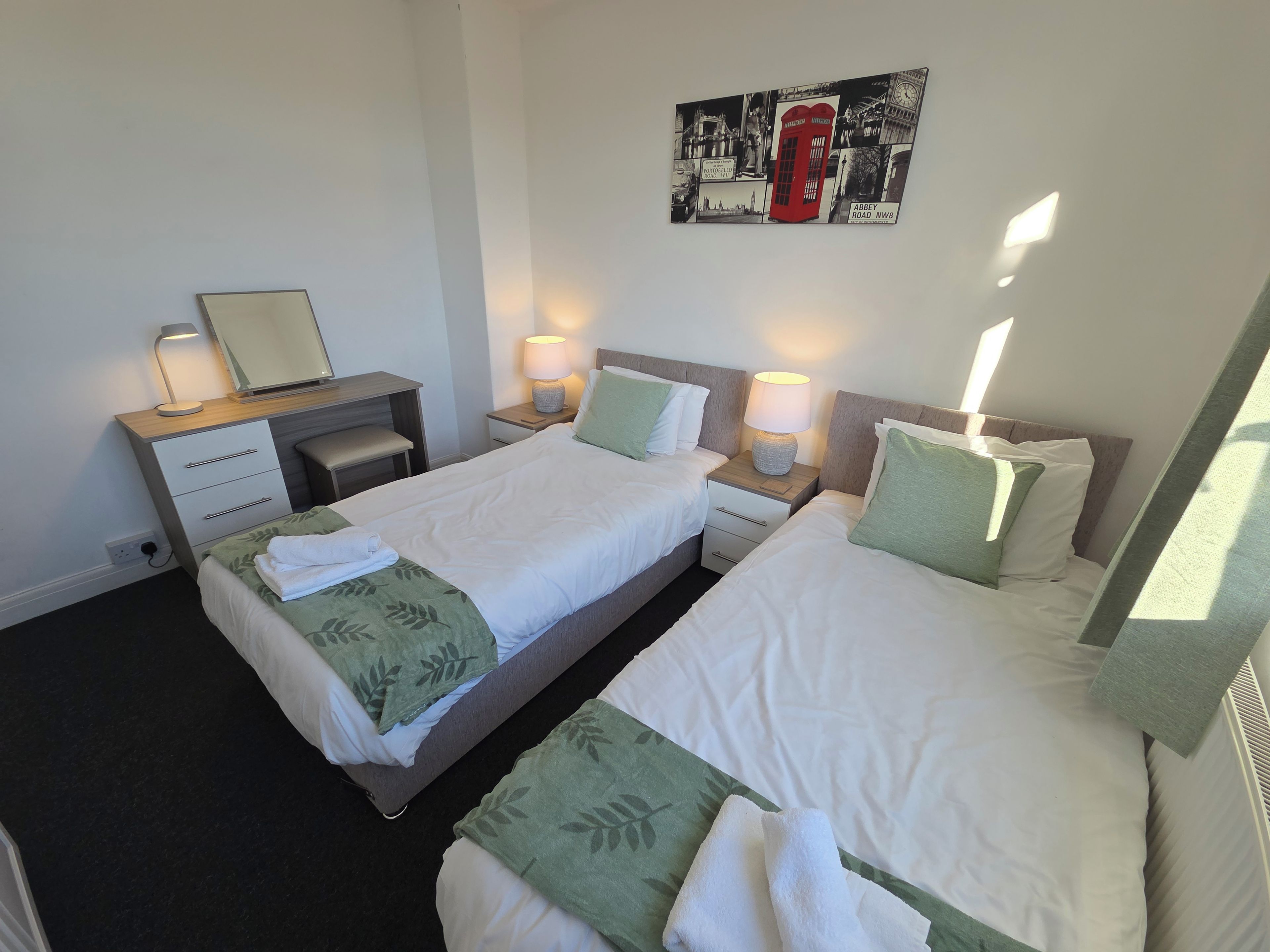 A hotel room with two beds, a desk, a chair, and a wall art piece.