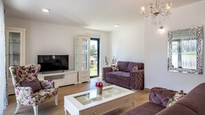 Een woonkamer met een televisie, een bloemenstoel, een bank en een glazen salontafel.