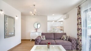 Een moderne woonkamer met een bank, een salontafel, een kroonluchter en een keuken op de achtergrond.