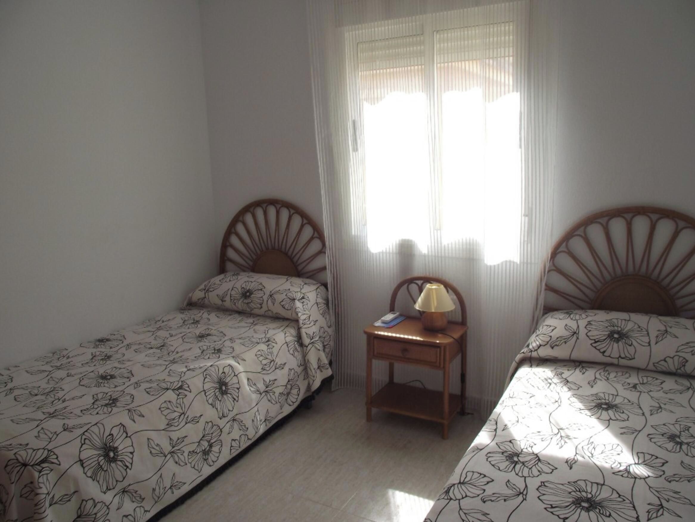 A bedroom with two single beds, a nightstand with a lamp, and a window with blinds.