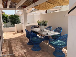 Un patio al aire libre con una mesa y sillas azules, rodeado de paredes blancas y plantas en macetas.