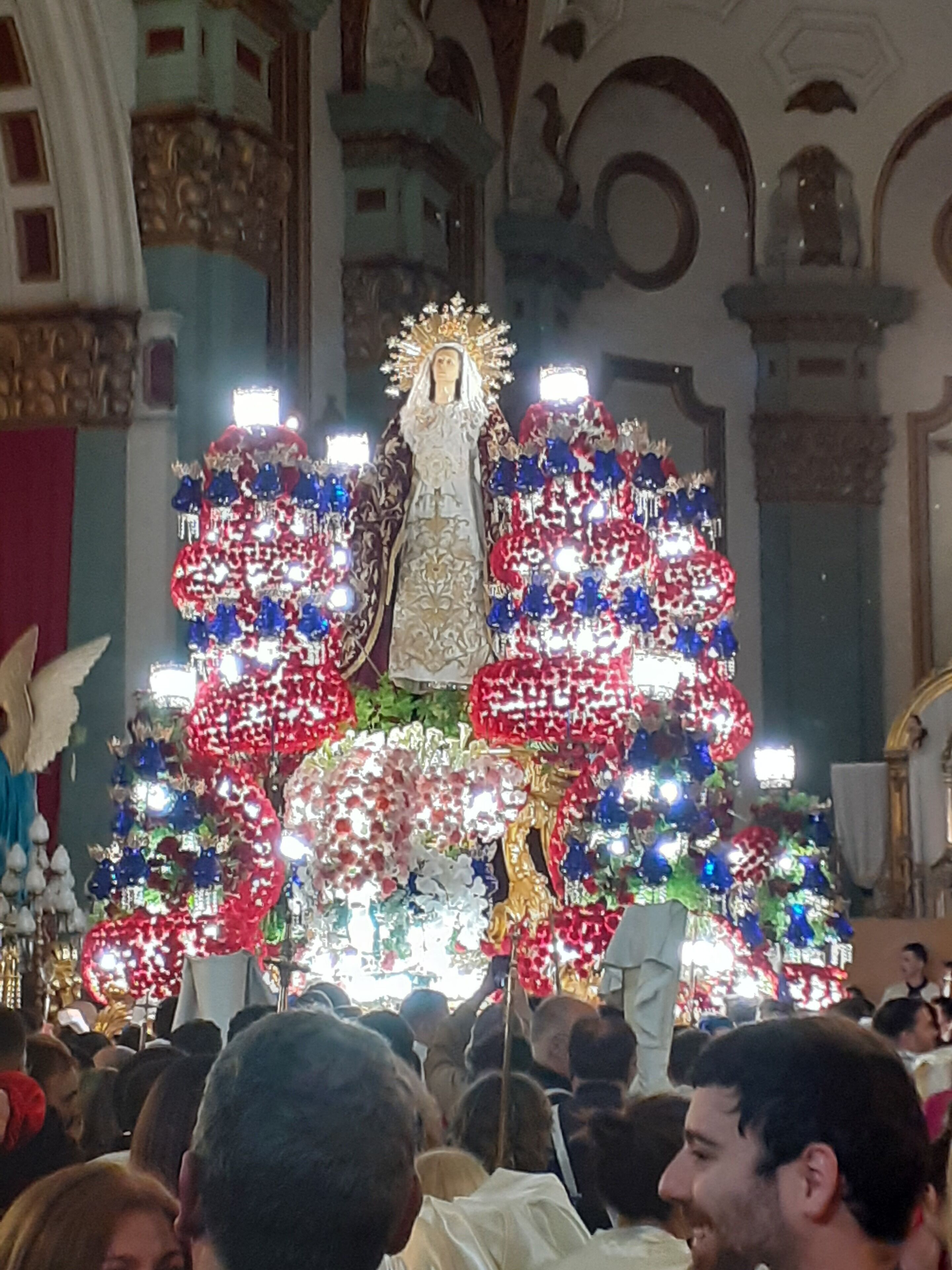 A religious statue with a halo, surrounded by a crowd of people.