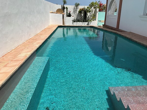 Una piscina con agua azul cristalina, rodeada de muros blancos y un suelo de baldosas.