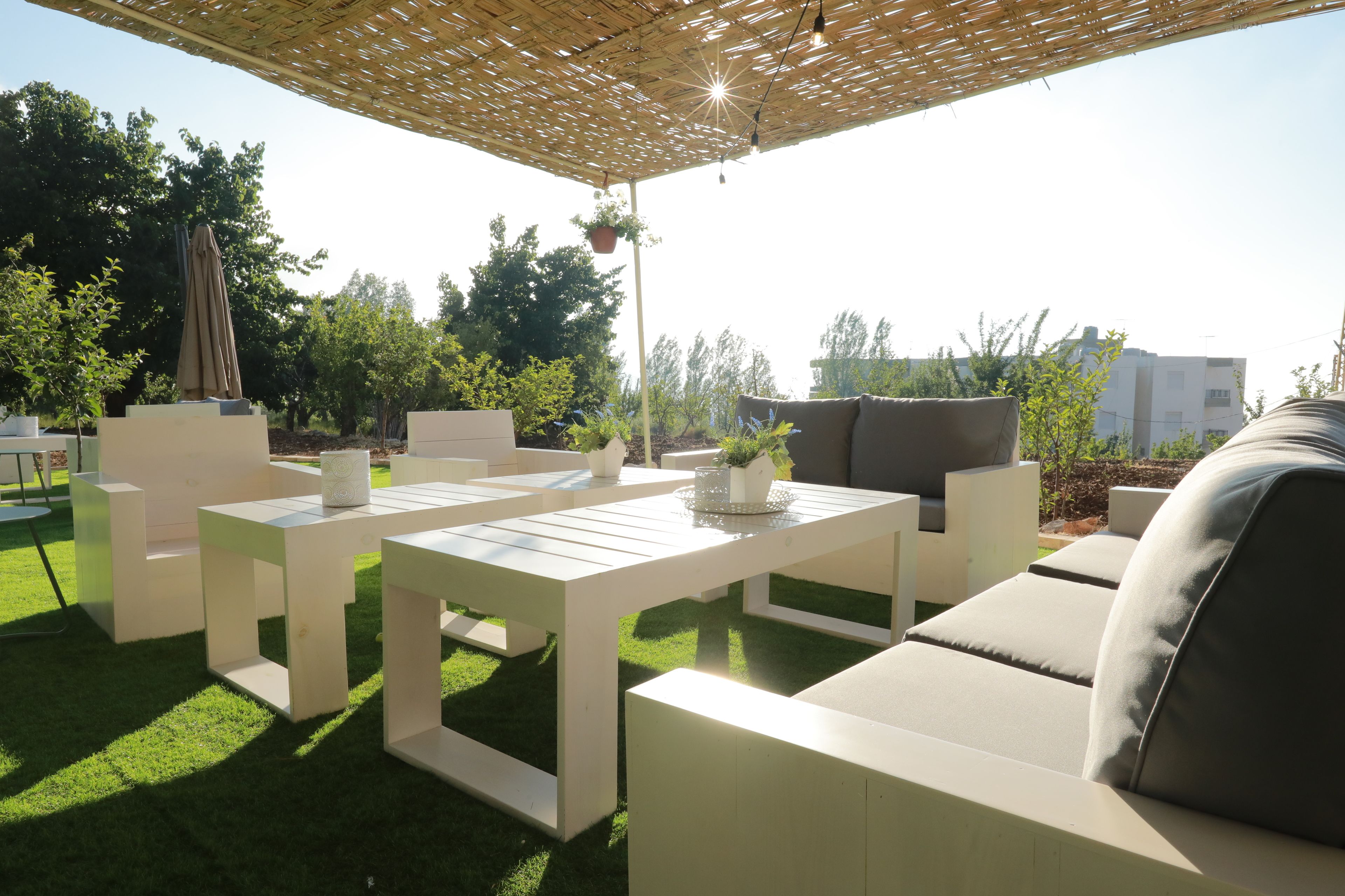 An outdoor seating area with white furniture, a pergola, and potted plants.