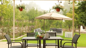 An outdoor patio with a table and chairs, a hanging planter, and a large umbrella. - Beit Mirna Guesthouse & Chalet (Ehden)