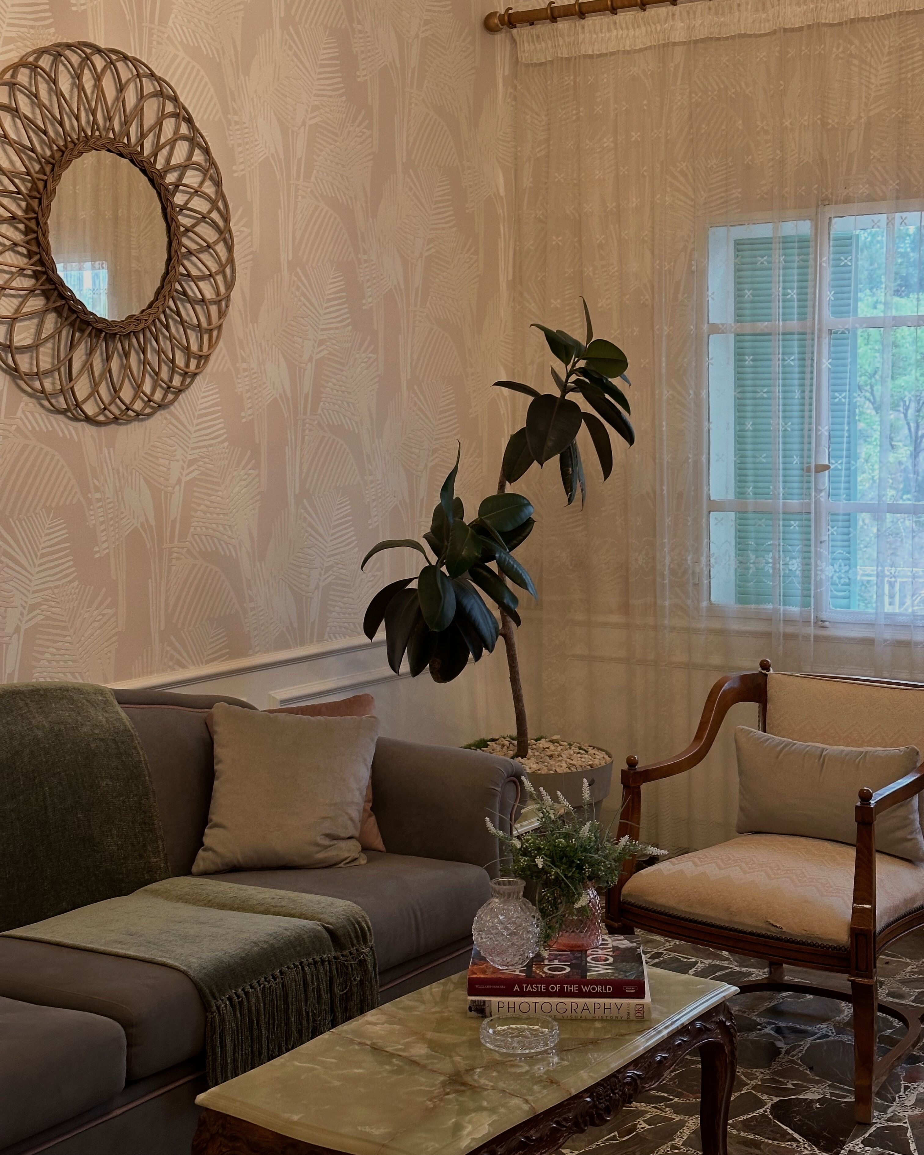 A living room with a sofa, armchair, coffee table, decorative mirror, and a potted plant.