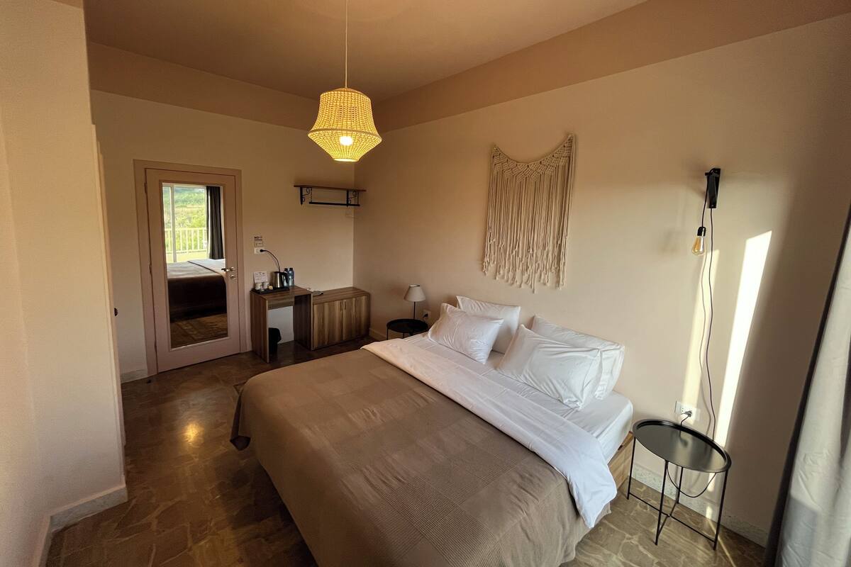 A bedroom with a bed, bedside table, lamp, and a macrame wall hanging.