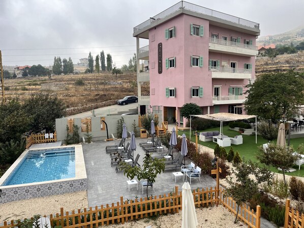 A pink multi-story building with a pool and outdoor seating area.