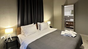 A hotel room with a bed, a nightstand with a lamp, a mirror, and a bathroom visible through an open door. - Beit Mirna Guesthouse & Chalet (Ehden)