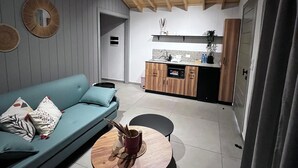 A modern living room with a blue sofa, a round wooden coffee table, and a kitchen area with wooden cabinets and a countertop. - Beit Mirna Guesthouse & Chalet (Ehden)
