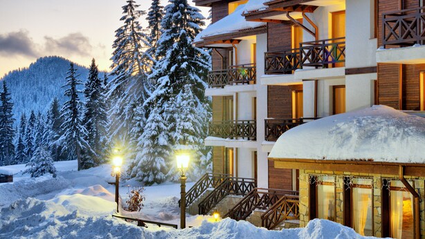 Un edificio de varios pisos con balcones, rodeado de árboles nevados y un paisaje cubierto de nieve.