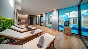 Zona de spa con camillas de masaje, un pequeño rincón de café y vistas a una piscina interior.