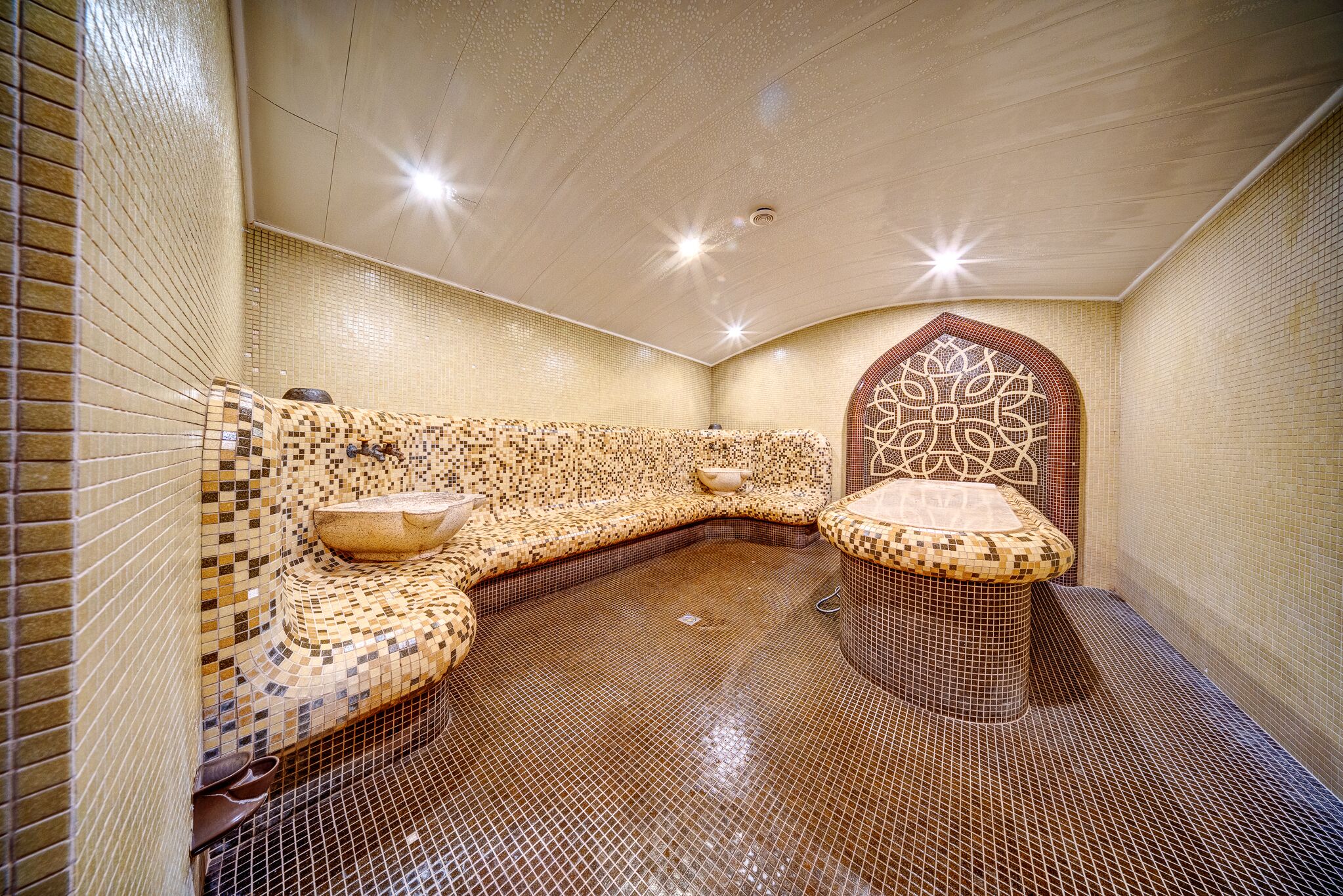 A spa room with mosaic tile walls, a curved bench, and a decorative arch.