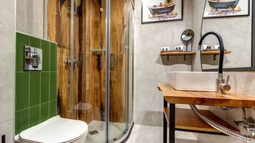 Un baño moderno con ducha envuelta en vidrio, inodoro blanco y tocador de madera con lavamanos y espejo.