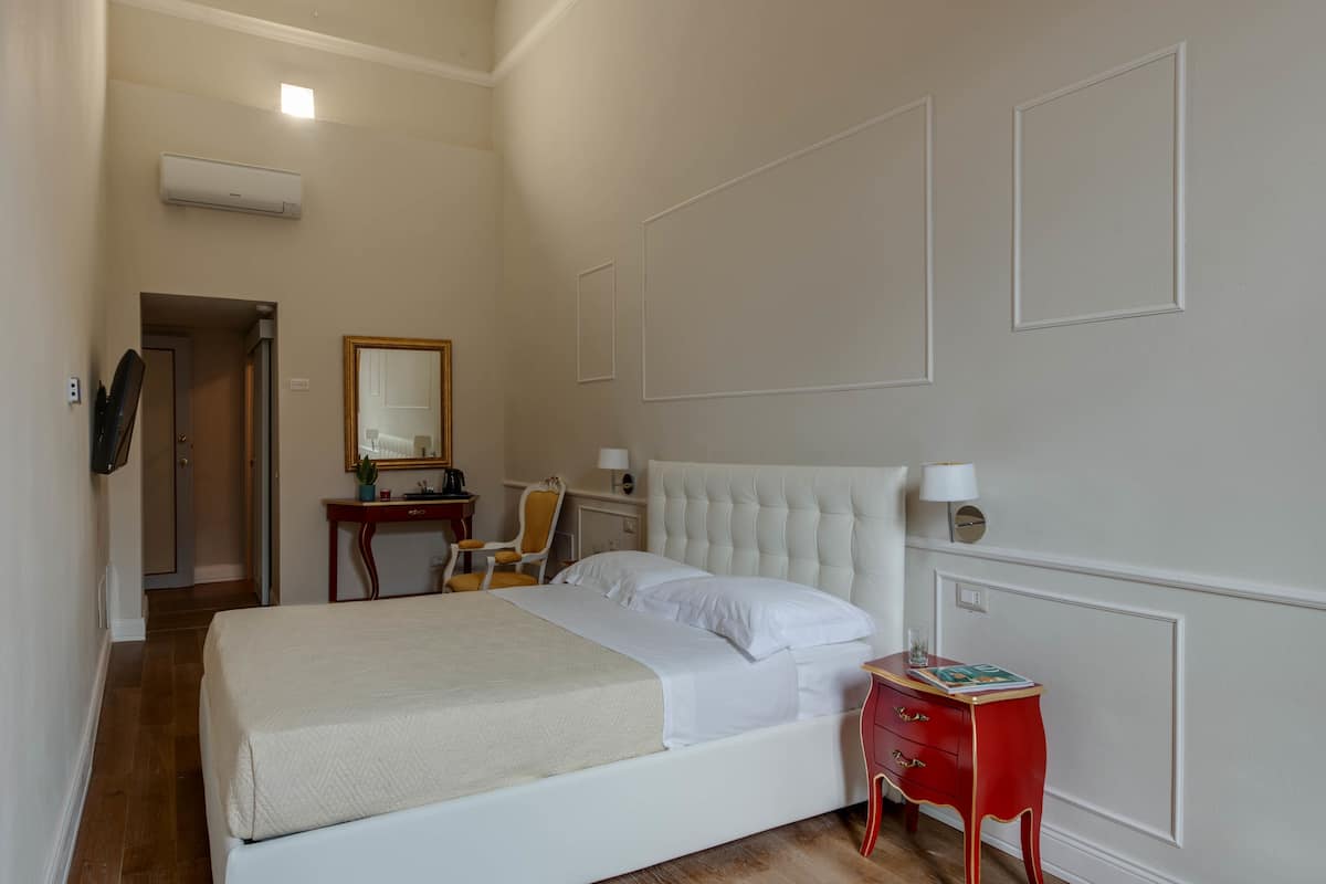 Een slaapkamer met een groot bed, een rode nachtkastje, een spiegel en een deur naar een andere kamer.