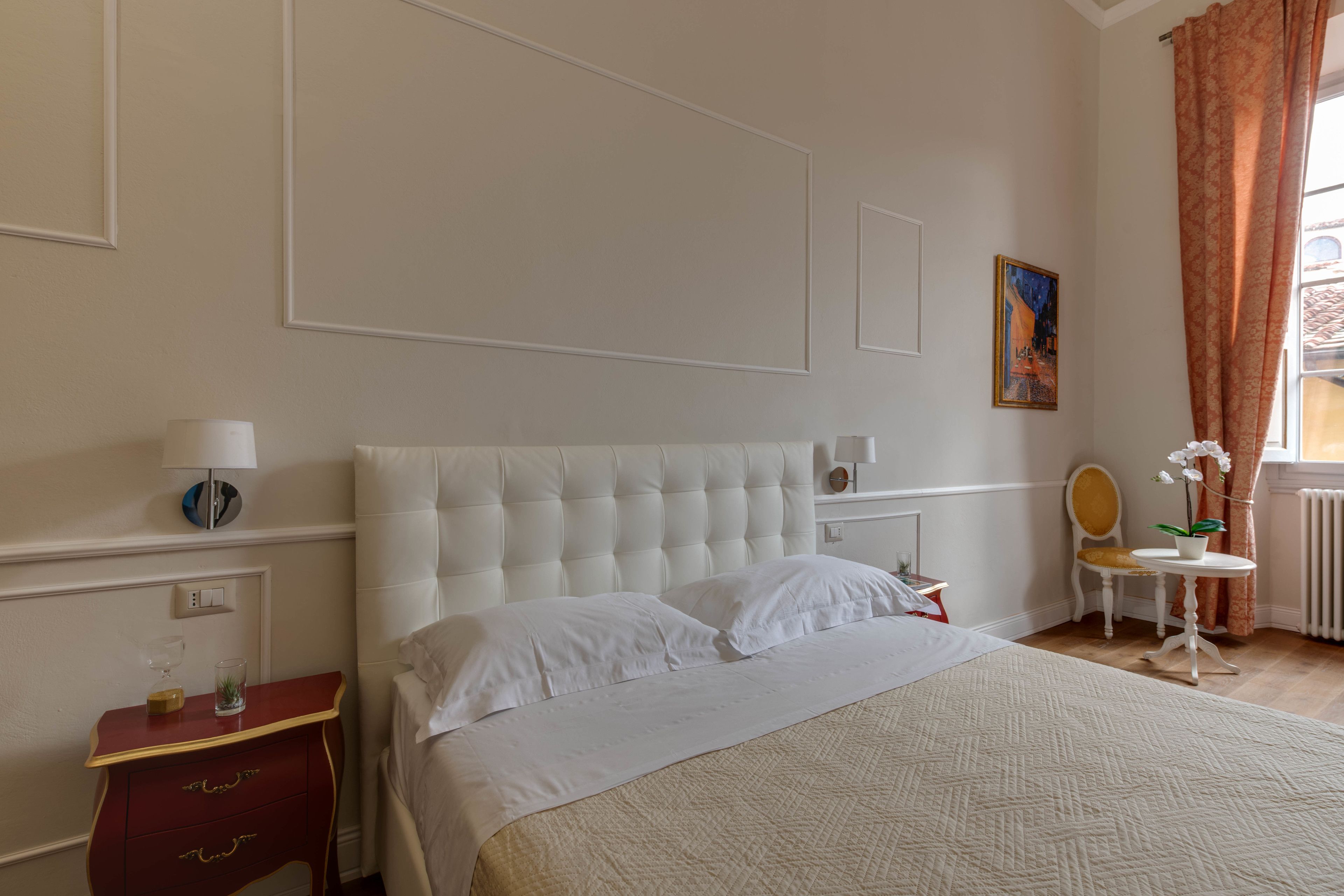 A neatly arranged bedroom with a large bed, a bedside table, a small table with a plant, and a chair.