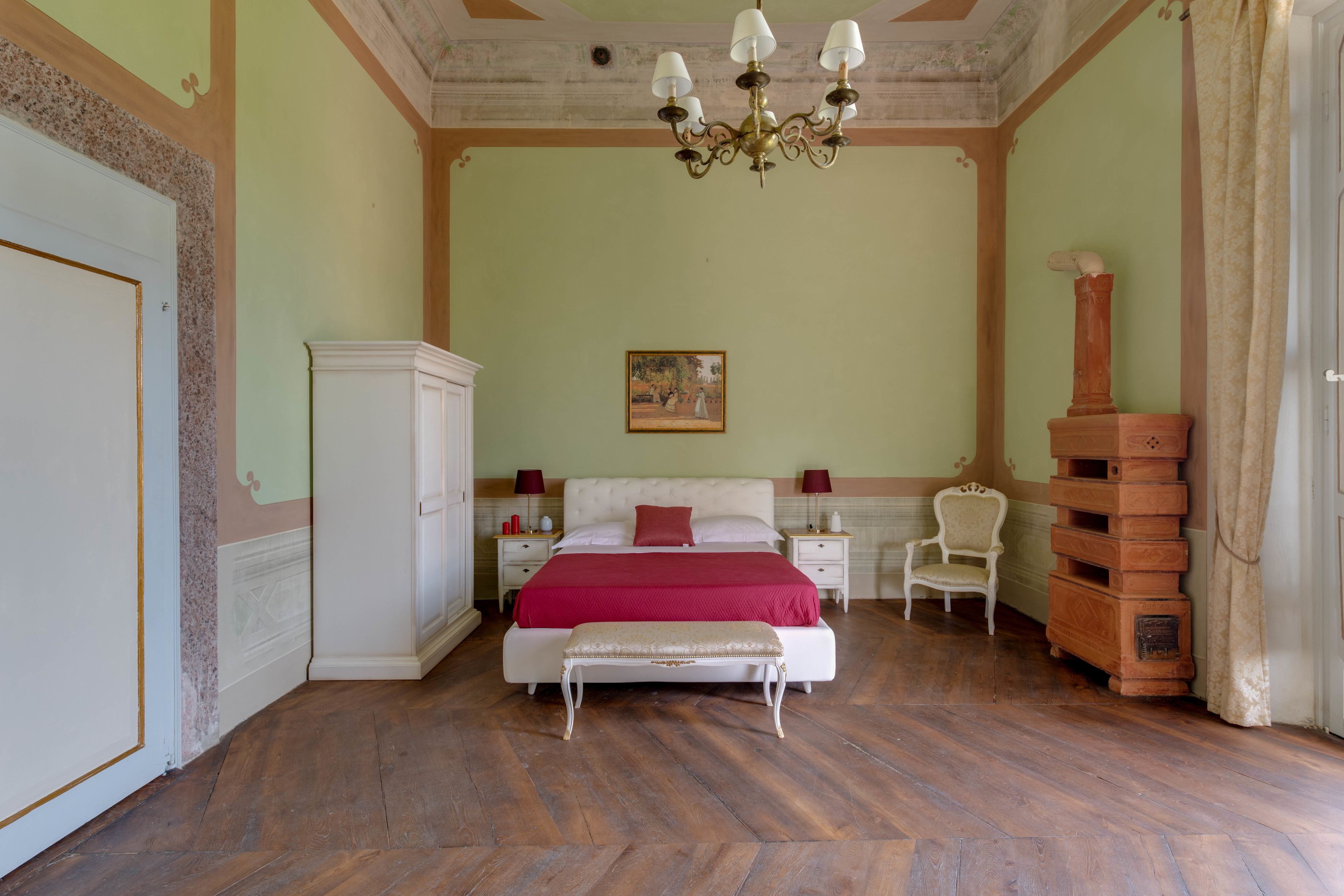 Un dormitorio con una cama grande, un banco, una silla, una mesita de noche y un pilar decorativo.