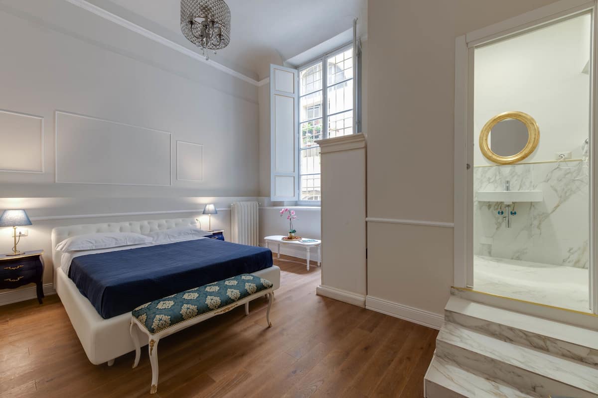 Een slaapkamer met een bed, nachtkastje, lamp en een raam met uitzicht.