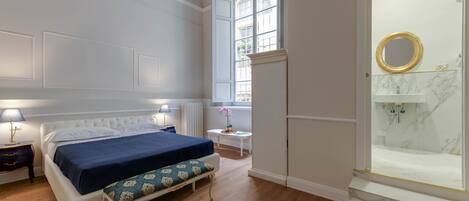 A bedroom with a bed, bedside table, lamp, and a window with a view.