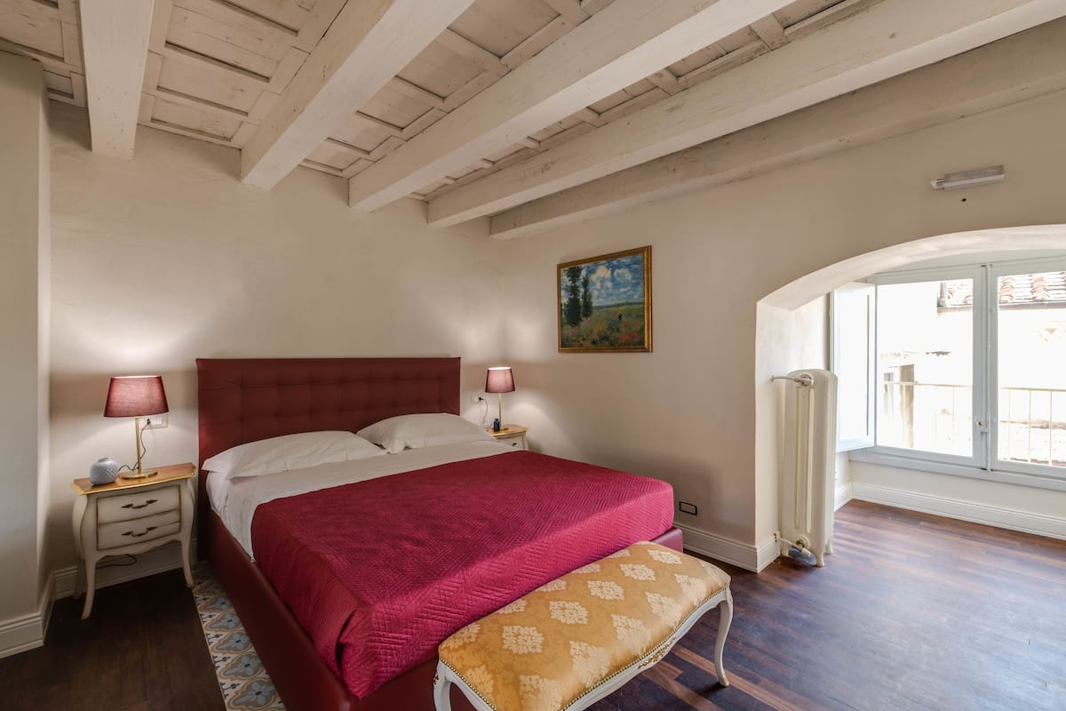Een slaapkamer met een groot bed, twee nachtkastjes met lampen, een bankje, een radiator en een raam met uitzicht.
