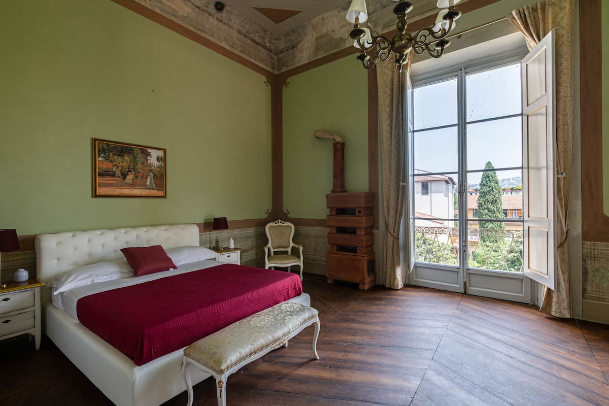 Een slaapkamer met een groot bed, een bankje, een stoel, een houten kast en een schilderij aan de muur.