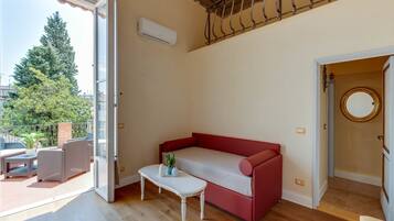 Una habitación con un sofá rojo, una mesita con una planta y vistas a árboles y edificios.