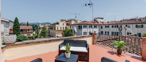 A rooftop terrace with wicker furniture, potted plants, and a clear view of the cityscape.