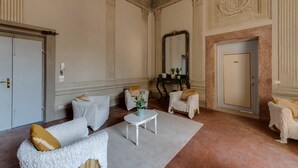 Une pièce spacieuse avec un plafond haut, des moulures décoratives, un grand miroir et une porte dotée d’un cadre ornemental.