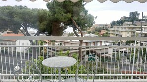 Un balcon avec deux chaises en métal et une petite table, donnant sur un quartier résidentiel avec des immeubles et des arbres.
