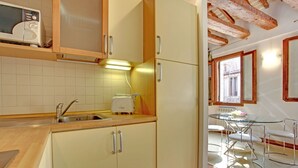 A kitchen with wooden cabinets, a toaster, and a sink. There is a dining area with a glass table and metal chairs. - Grimaldi Apartments - Ca Orlina (Venice)