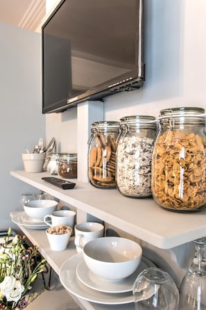 A breakfast bar with jars of cereal, bowls, and a remote control. - April House Weybridge - Boutique Guesthouse (Weybridge)