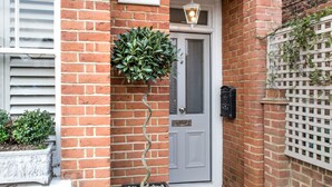 A brick building with a white door labeled "April House," a potted plant, and a white lattice fence. - April House Weybridge - Boutique Guesthouse (Weybridge)