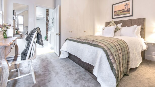 A bedroom with a bed, a nightstand, a lamp, a painting, and a door leading to a bathroom. - April House Weybridge - Boutique Guesthouse (Weybridge)