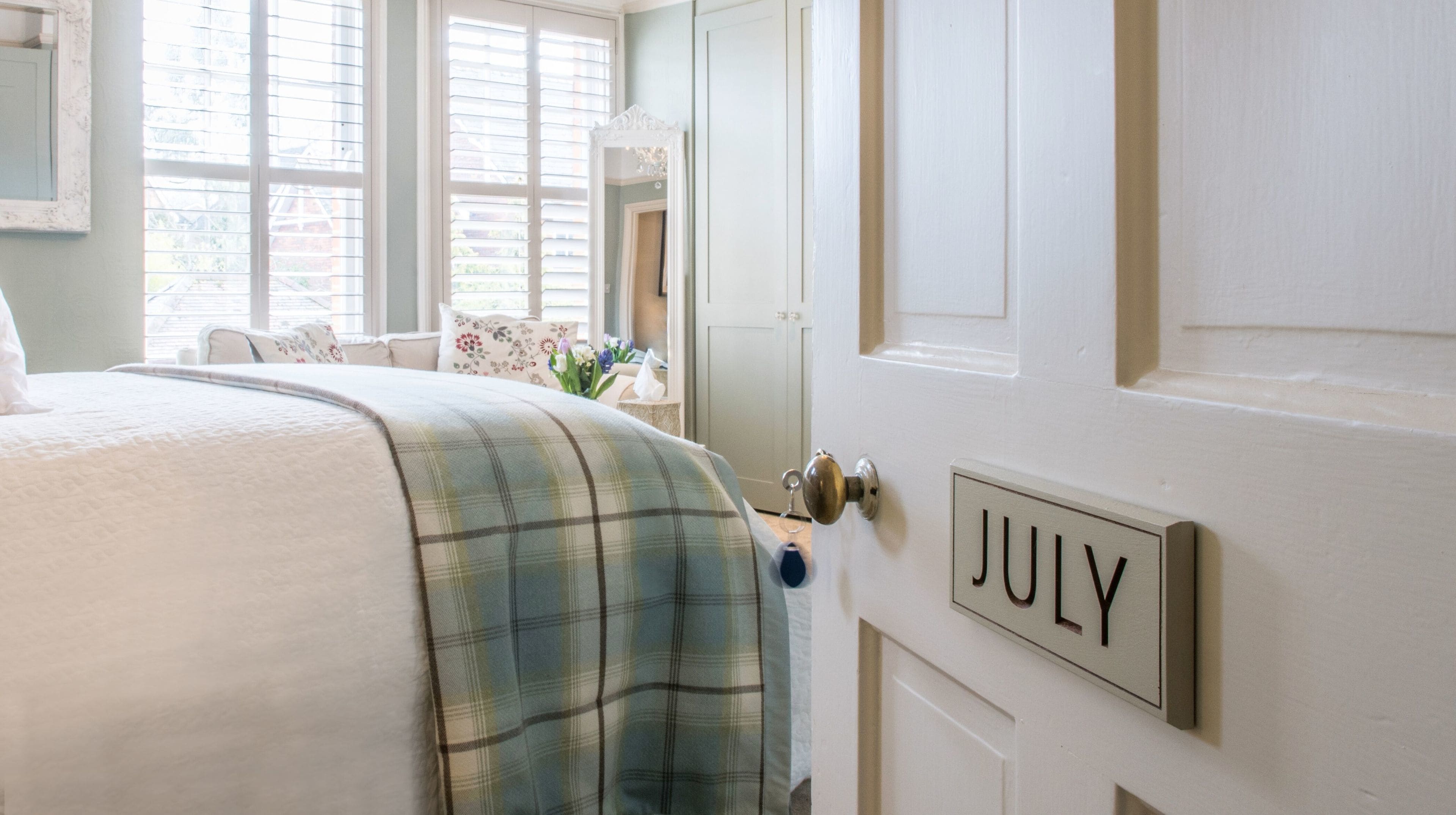 A bedroom with a bed, a door labeled "JULY", and a window with blinds.