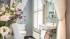 A bathroom with a toilet, sink, and shower. There is a vase with flowers on the left. - April House Weybridge - Boutique Guesthouse (Weybridge)