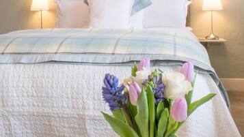 Un dormitorio con cama, almohadas, una mesita de noche con lámpara y una pared decorada con cuadros.
